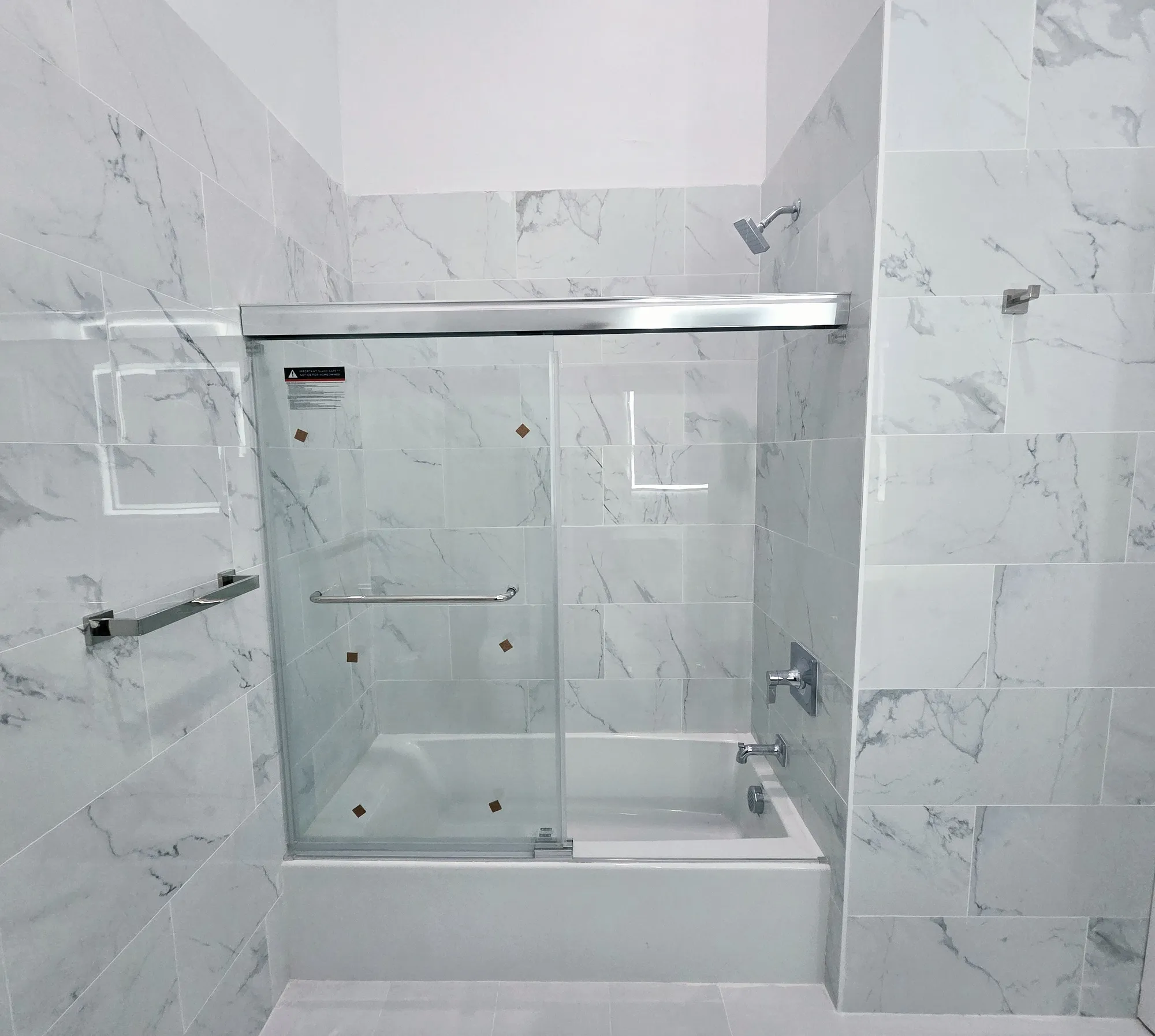 Bathtub with sliding glass doors surrounded by marble-pattern tile