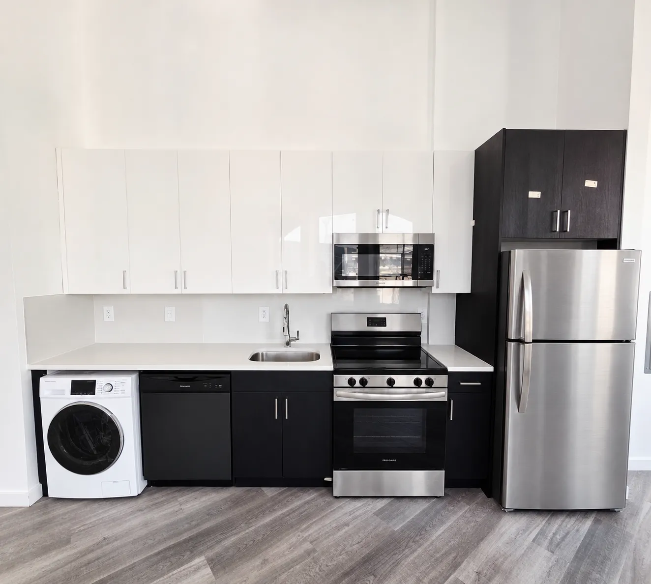 New apartment kitchen with white upper cabinets, black lower cabinets, quartz counters, and stainless appliances
