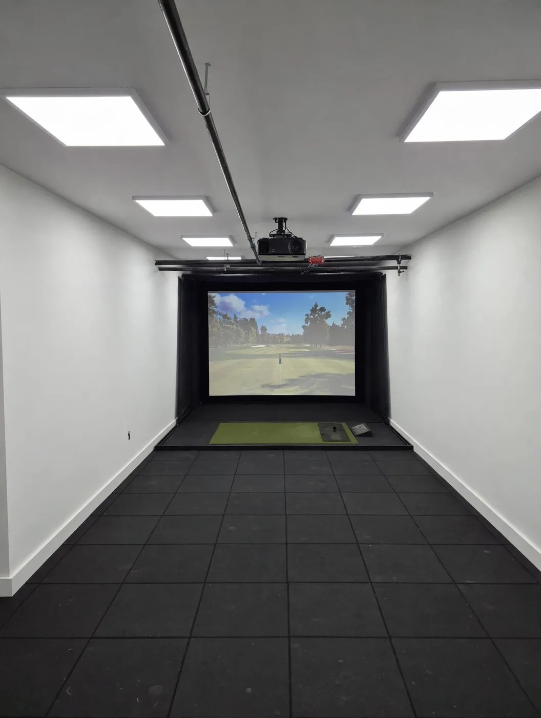 Sports simulator room with a golf course projected on a large impact screen and turf hitting mat